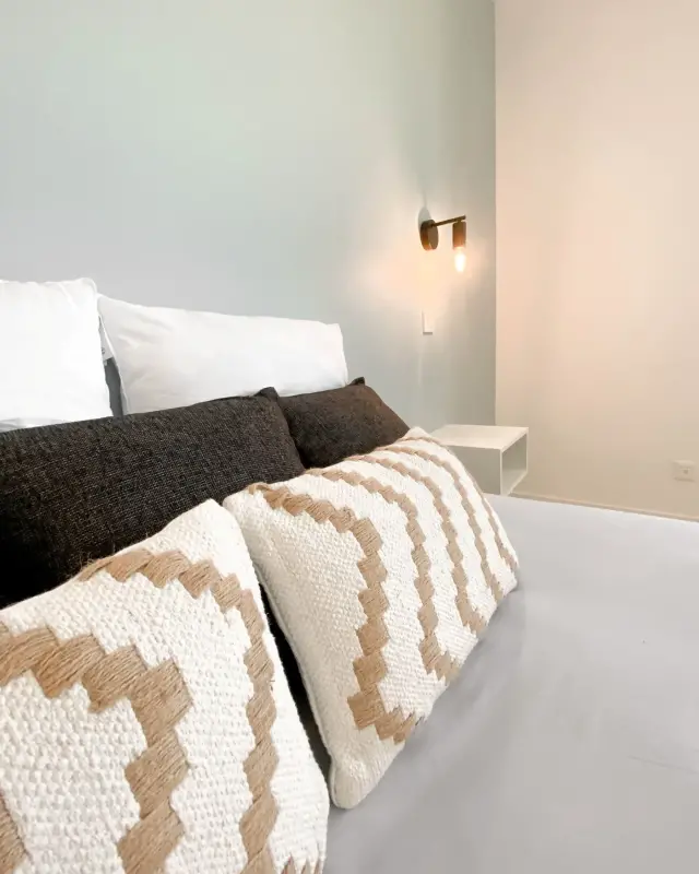 Lit avec coussins tissés beige et brun, mur vert de gris et applique en laiton