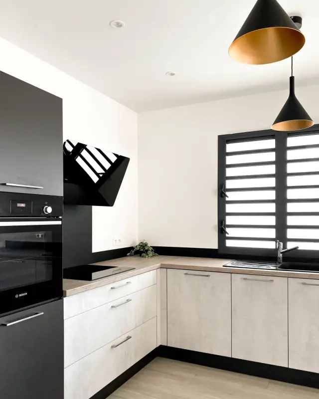 Suspensions coniques noires à intérieur doré au-dessus d’une cuisine effet béton et anthracite