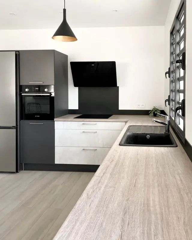 Plan de travail effet bois grisé, évier noir et fenêtre à lames orientables