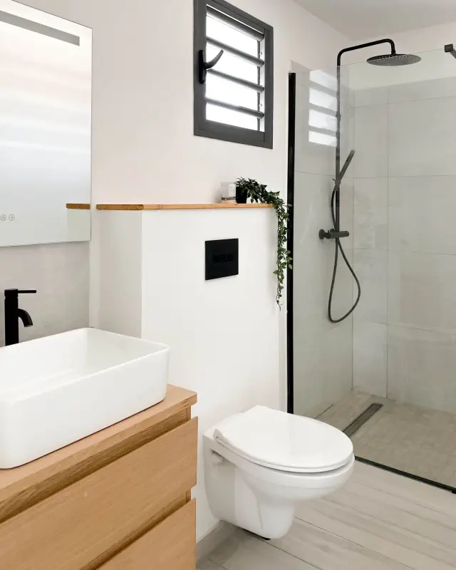 Salle d’eau avec meuble suspendu en bois, vasque blanche, WC suspendu et douche à l’italienne