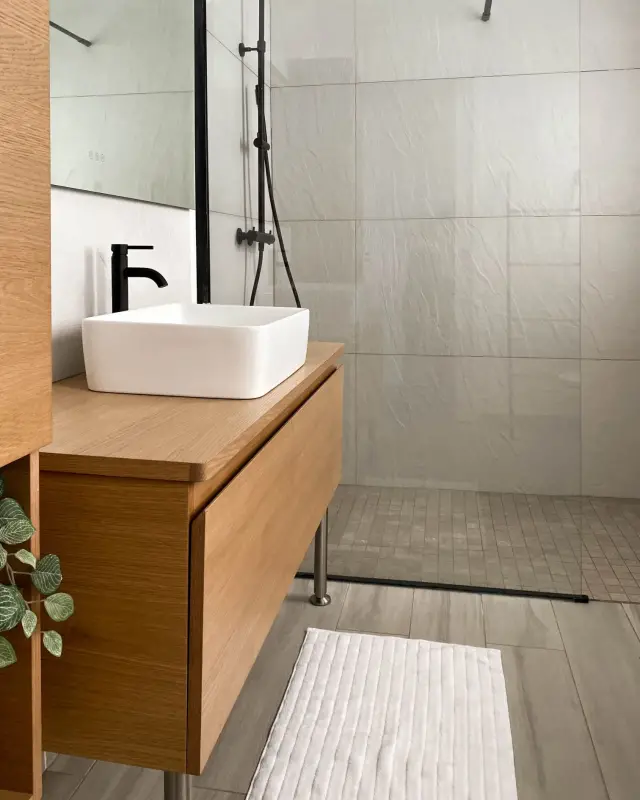 Vasque à poser blanche et robinet noir sur meuble suspendu en bois, douche vitrée à profil noir