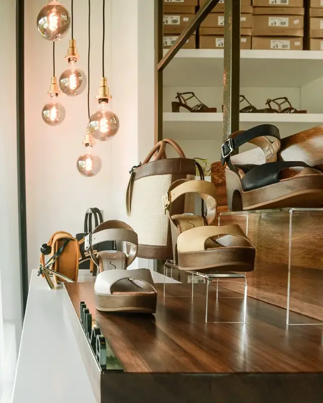 Ampoules globe à filament au-dessus d’un podium en bois présentant sandales et sacs