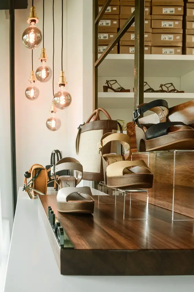 Vitrine de la boutique Chaus’en Folie à L’Ermitage-les-Bains : sandales présentées sur un plateau en bois sous des suspensions à ampoules