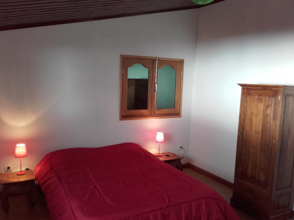 Chambre double à l'étage avec sa couette rouge et son armoire en bois