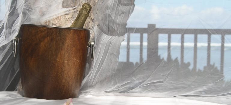 Bouteille de champagne au frais dans un seau en bois, face au lagon