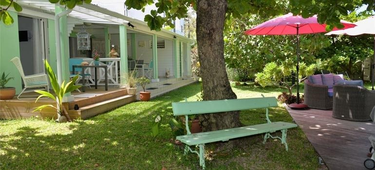 Maison aux varangues vert d'eau et pelouse ombragée par un grand arbre