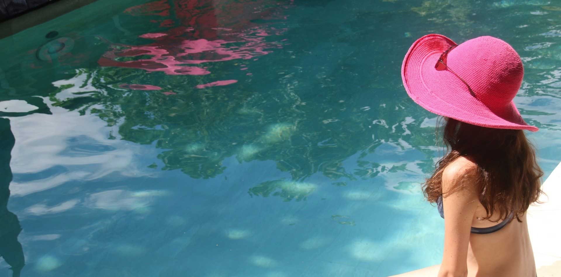 Femme au chapeau rose au bord de la piscine émeraude