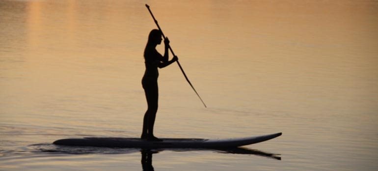 Silhouette d'une paddleuse sur le lagon au coucher du soleil