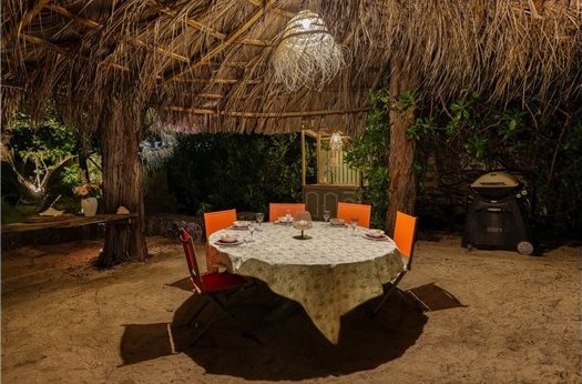 Table ronde dressée le soir sous la tonnelle en feuilles de cocotiers, avec la cuisine extérieure