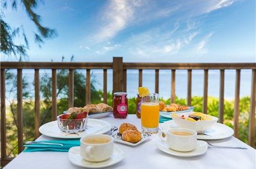 Petit déjeuner servi face à la mer : viennoiseries, jus d'orange, confitures et café
