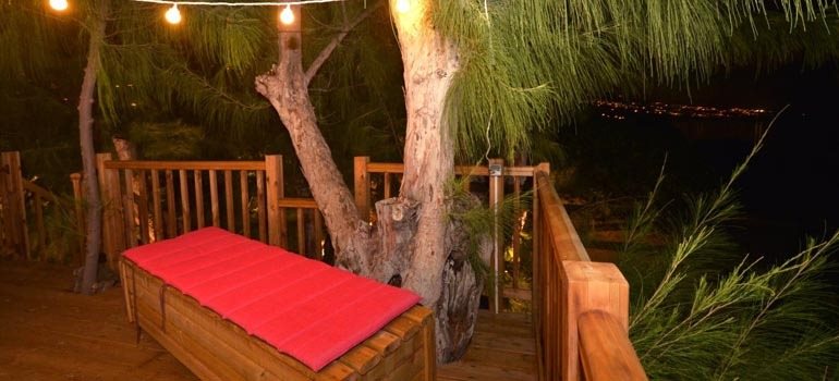 Terrasse dans les arbres illuminée par une guirlande lumineuse le soir