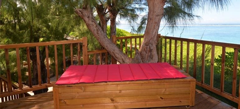 Banquette sur la terrasse en bois entre les troncs de filaos, vue sur la mer