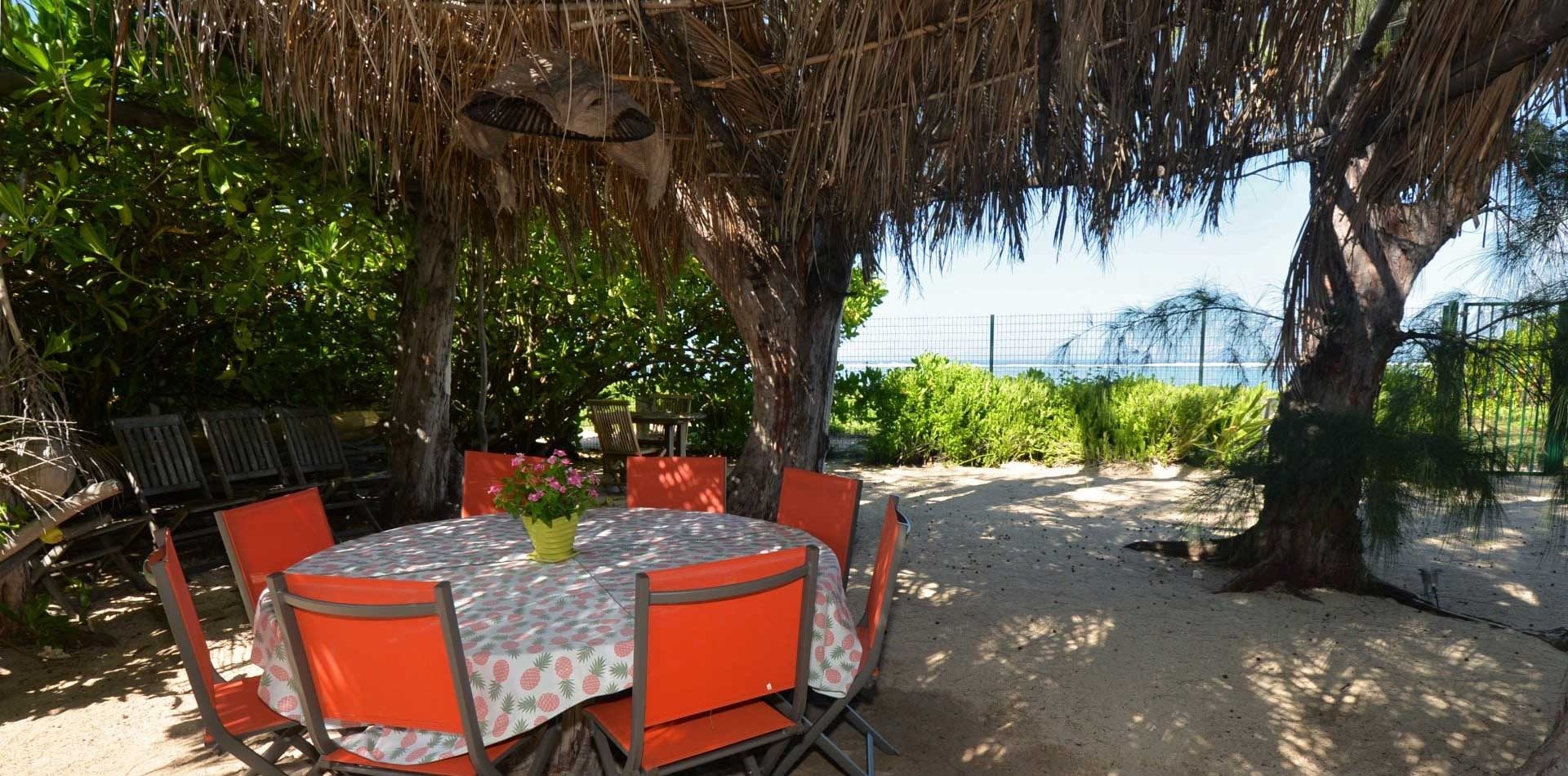Table ronde sous la tonnelle en feuilles de cocotiers, entre les filaos et la plage