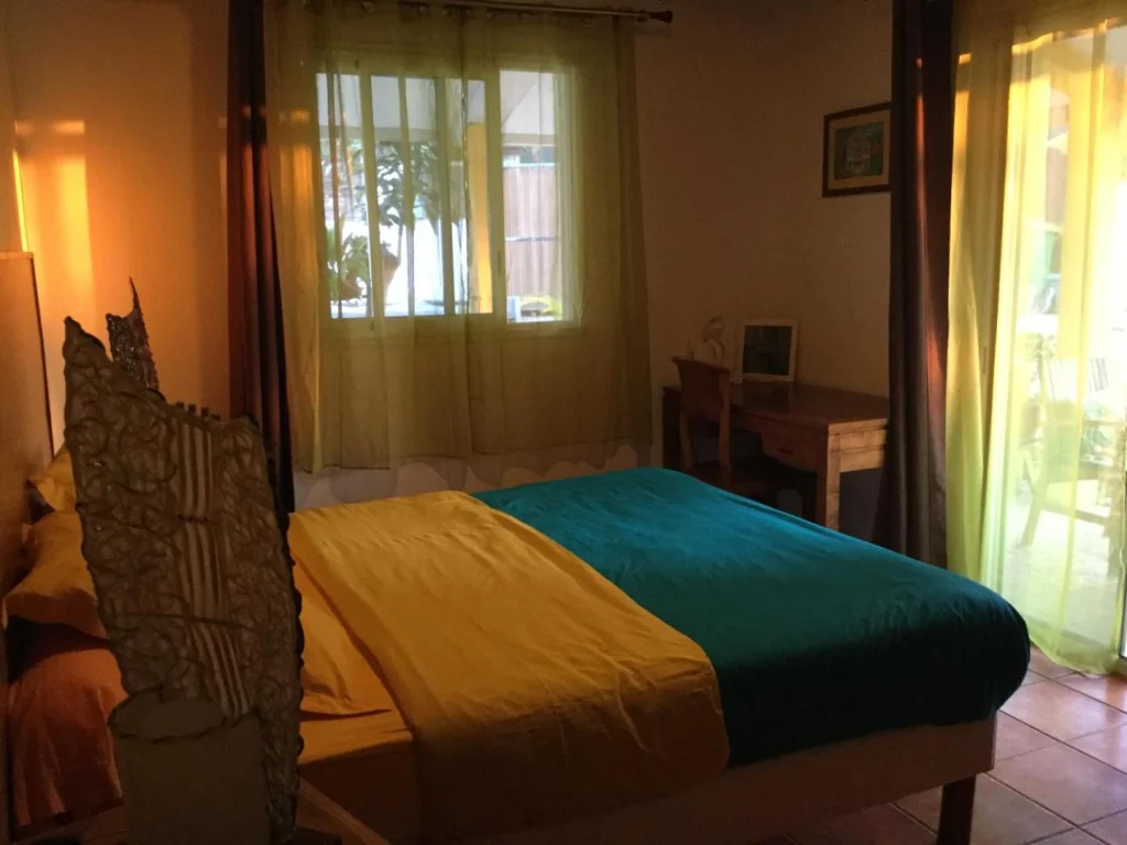 Chambre Terrasse : lit double, tête de lit en bois sculpté et linge jaune et turquoise, chambres d'hôtes Lé Fé Coco à Saint-Paul