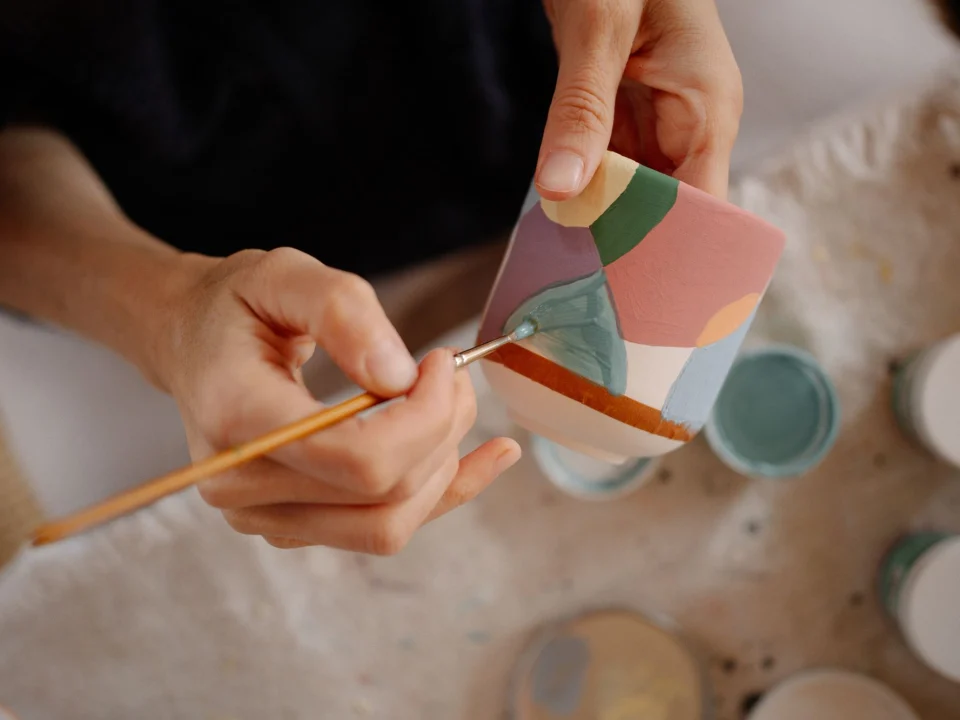 Mains qui peignent délicatement une petite pièce en céramique pastel
